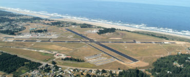 The aiport landing strips and ocean are shown beneath a plane's wing.