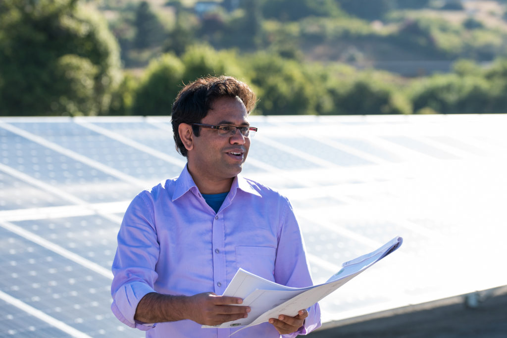 A graduate student engineer holds blueprints while standing next to a solar array
