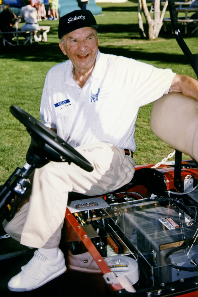 Louis Schatz, wearing a Schatz Center cap and shirt, sits on a fuel cell vehicle with the fuel cell shown.