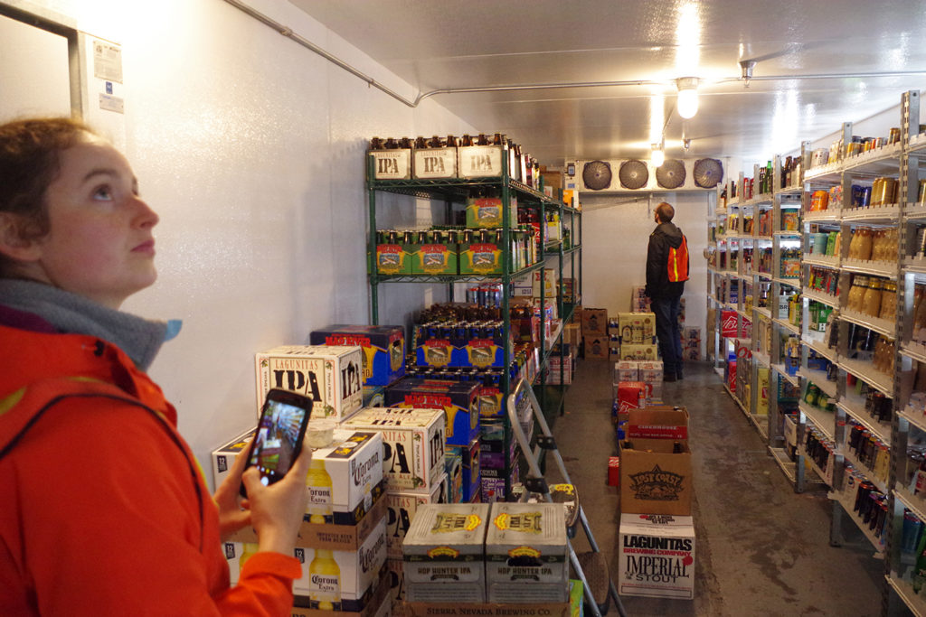 Two students in orange vests stand inside a convenience store refrigerator