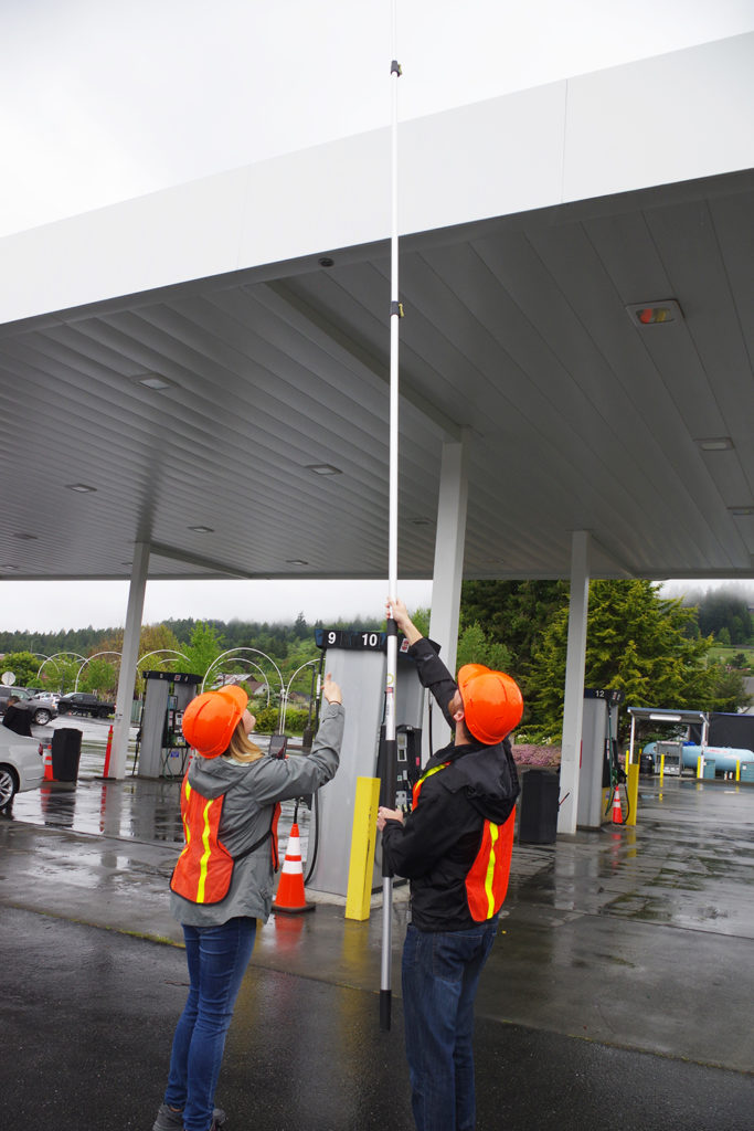 Two students use a GoPro on an extension pole to take canopy measurements at a fueling station