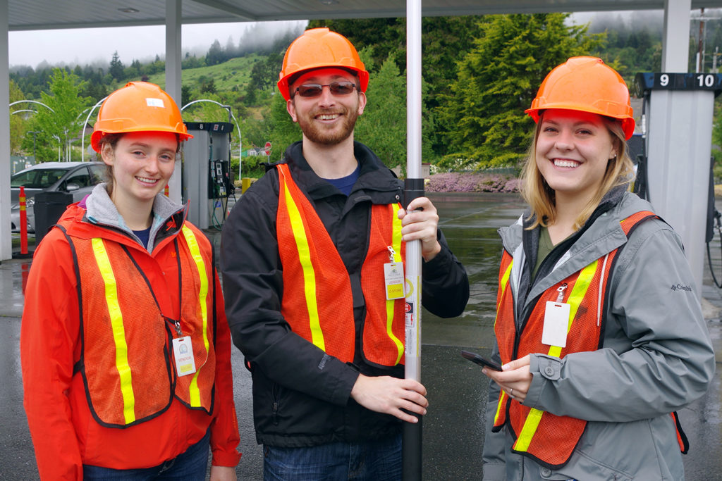 Three students in hardhats and orange vests just outside a gas station canopy