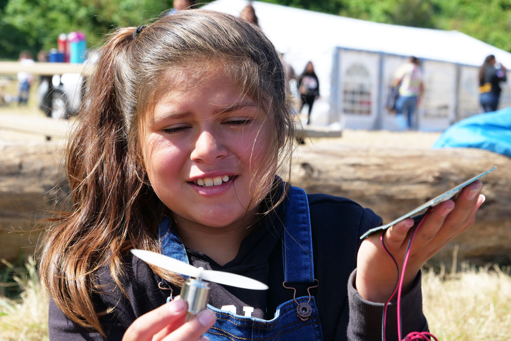 A girl holds a fan and a solar cell, connected by wires