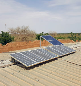A clinic worker stands on the roof beside a small solar array