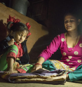 Ambika Parajuli holds a solar lamp to help her four year old daughter do homework.
