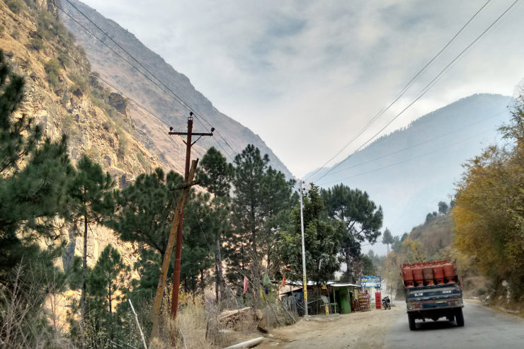A truck drives past a small roadway shop in the mountains, with power lines overhead.