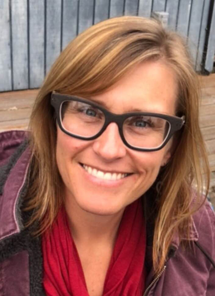 Author is outside near a gray fence, and is wearing a maroon coat