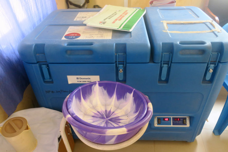 A blue, top-loading refrigerator with a manual on top sits behind nested purple and white plastic bowls and a tan plastic pitcher