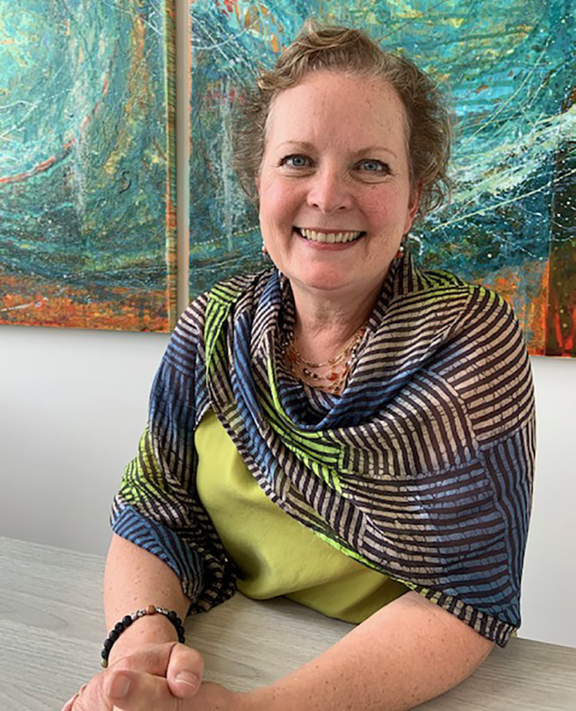 A smiling woman sits in front of a painting