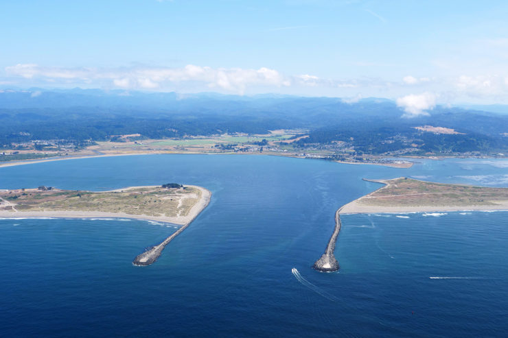 An aerial view of the entrance to Humboldt Bay, where a small boat enters between two jetties.