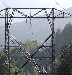 A closeup of a transmission tower between tree-covered hills