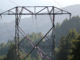 A closeup of a transmission tower between tree-covered hills