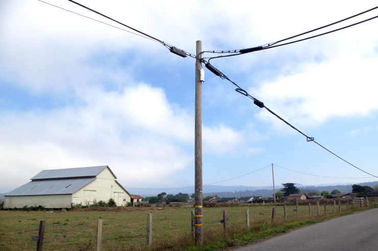 A utility pole in the foreground, with a barn in the background