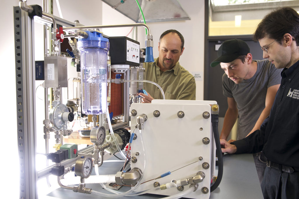 Three engineers look closely at a hydrogen fuel cell stack