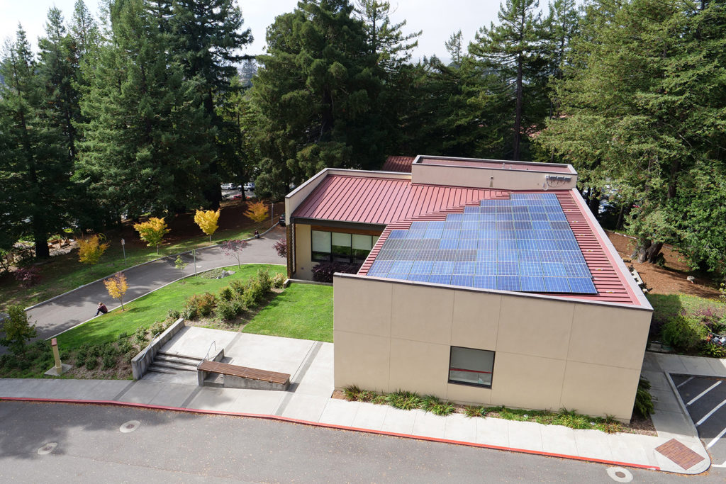 The Schatz Center as seen from the BSS building, ringed by redwoods and with a solar array on a pink-red roof.