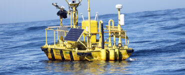A yellow buoy with multiple sensors floats in open sea