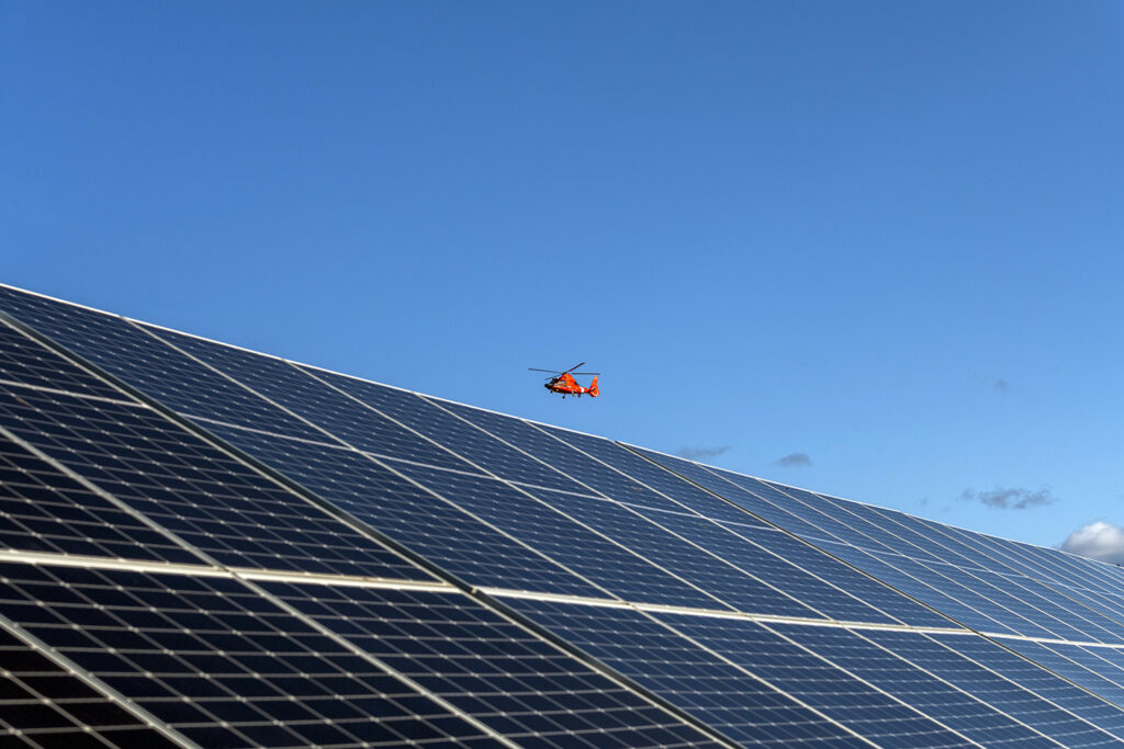 A Coast Guard helicopter flies above a solar array