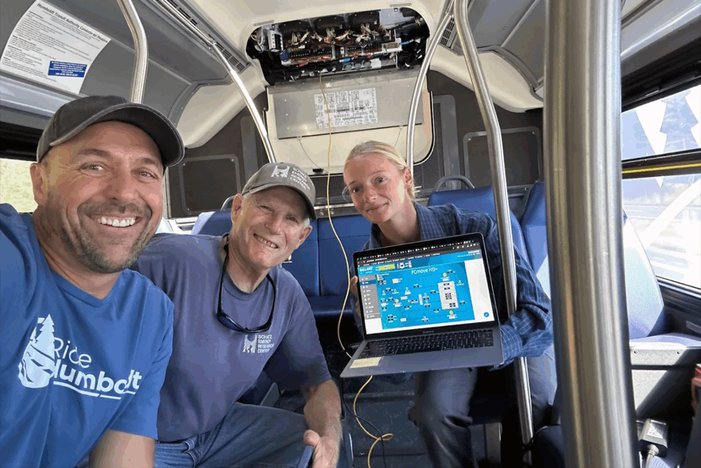 Three engineers sitting inside a bus show performance results during a live test of the 101 route.
