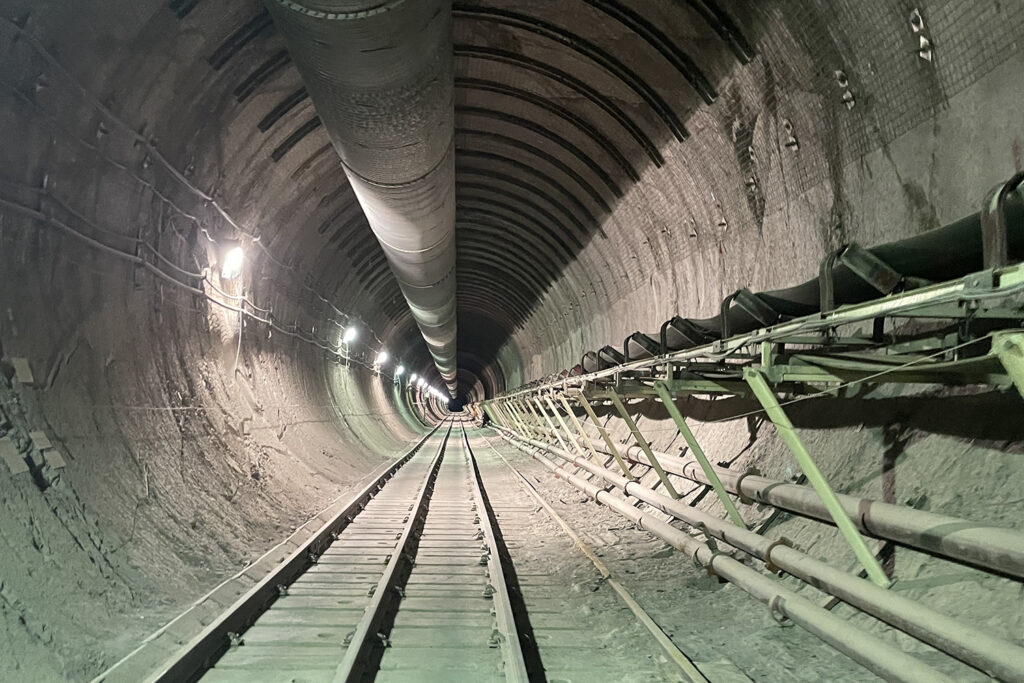 A long tunnel extends into the dark, with rail-tracks below and pipes above and to the right