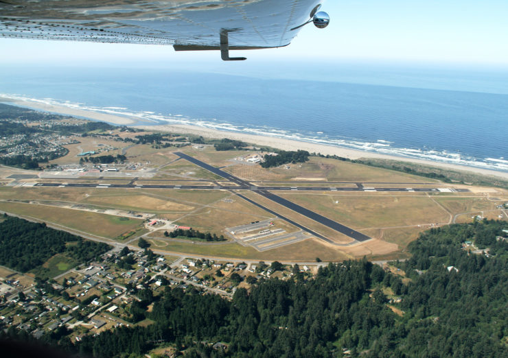 The aiport landing strips and ocean are shown beneath a plane's wing.