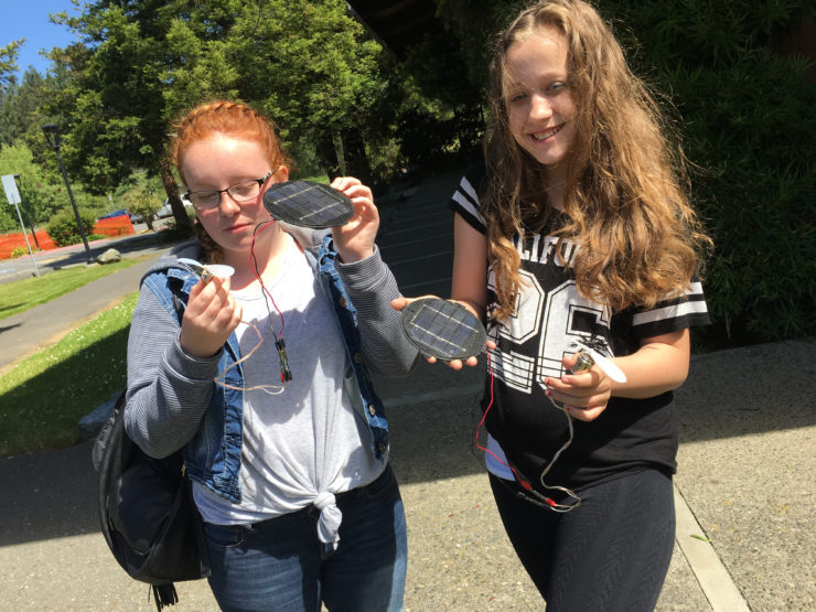 Two middle school students hold solar modules and fans in the sun.