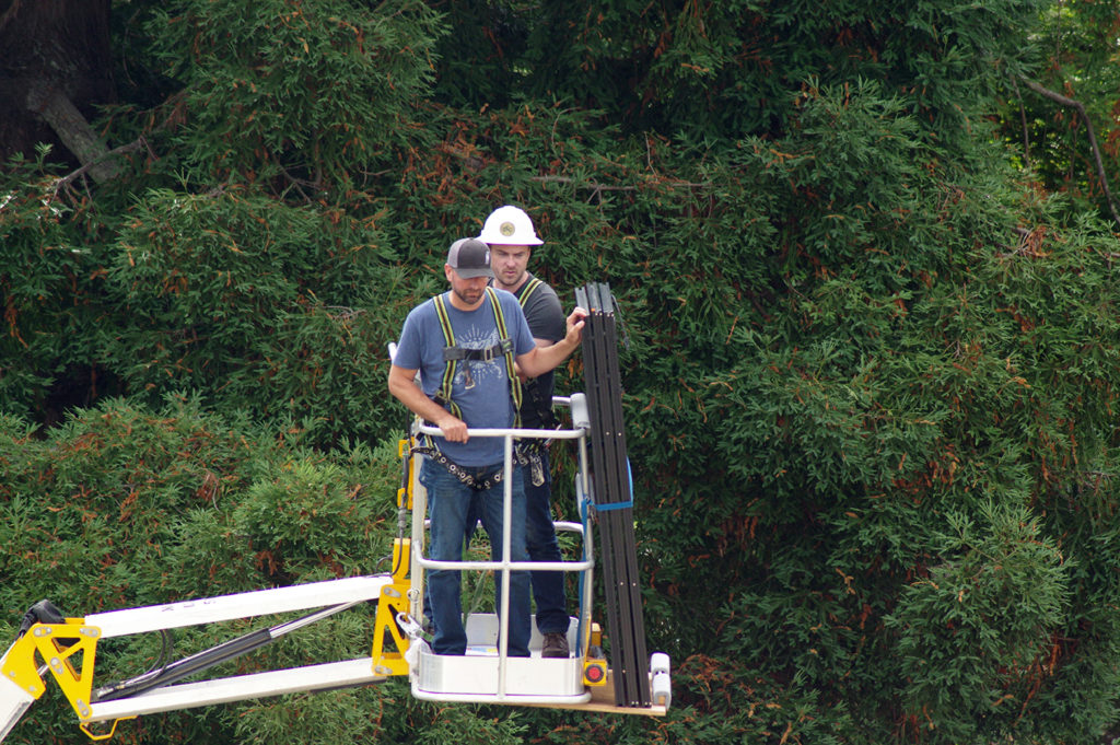 Travis and Ray transport panels in a hydraulic lift with redwoods behind