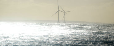 Light shines brightly over two offshore wind turbines and the ocean