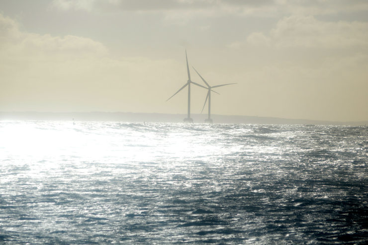 Light shines brightly over two offshore wind turbines and the ocean