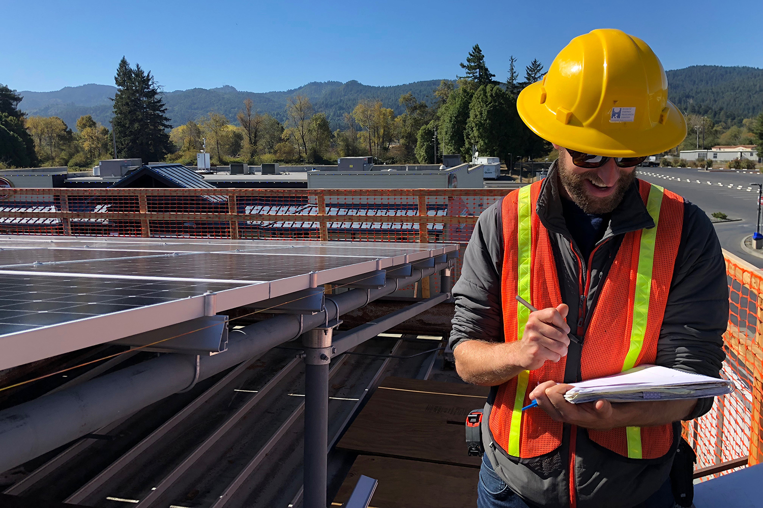 A student in a hardhat and safety vest stands next to a rooftop solar array