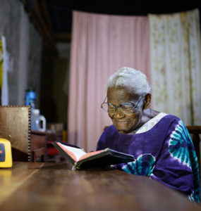 A elder woman reads at a dining room table by solar light