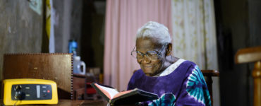A elder woman reads at a dining room table by solar light