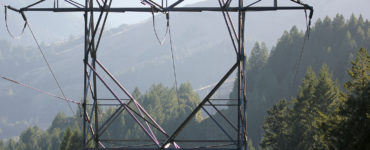 A closeup of a transmission tower between tree-covered hills