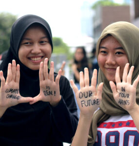 Two young women with "Climate Change is Real! Our future in your hands" written on their palms