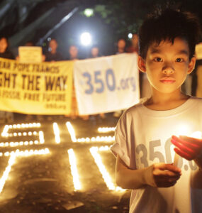 A child is holding a candle and wearing a shirt that says "350.org"