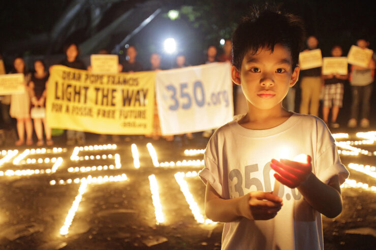 A child is holding a candle and wearing a shirt that says "350.org"