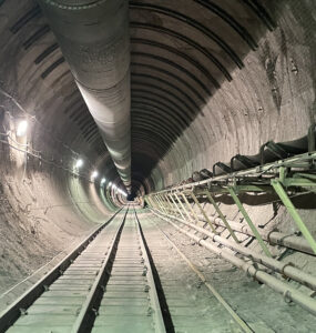 A long tunnel extends into the dark, with rail-tracks below and pipes above and to the right