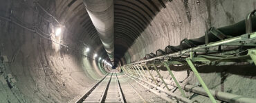 A long tunnel extends into the dark, with rail-tracks below and pipes above and to the right