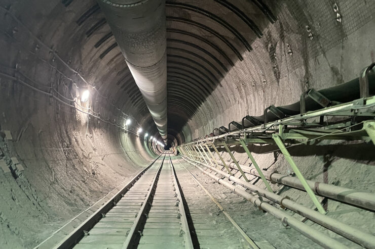 A long tunnel extends into the dark, with rail-tracks below and pipes above and to the right